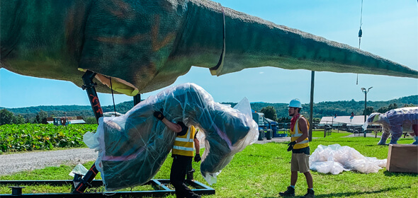 Two men in yellow vests are installing a 6-meter-tall green animatronic Tyrannosaurus Rex.