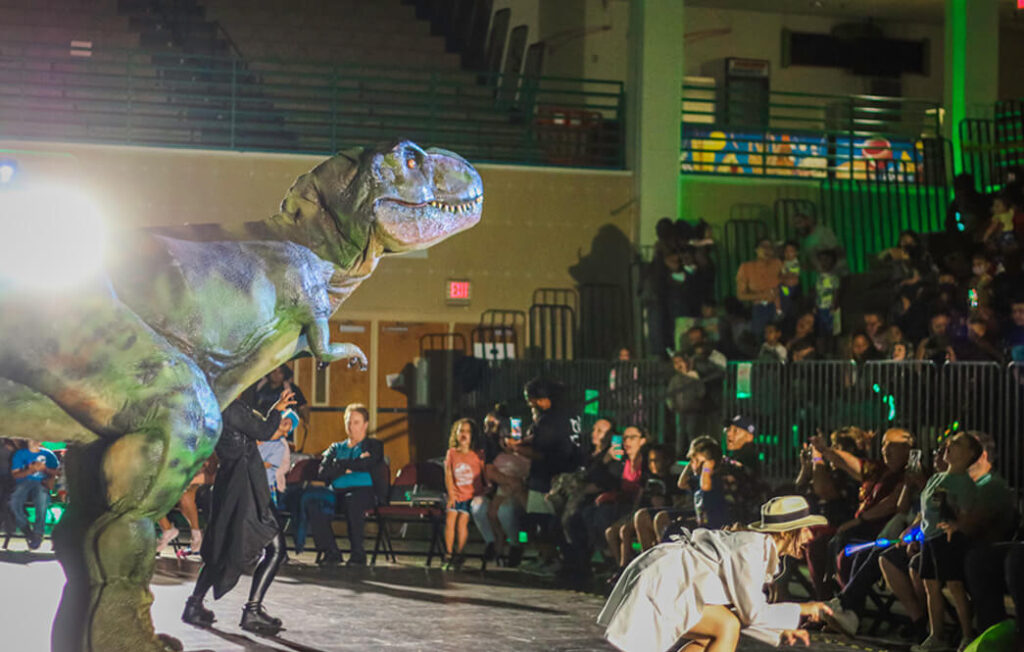 The girl in the apricot coat and the green Tyrannosaurus Rex are performing on stage