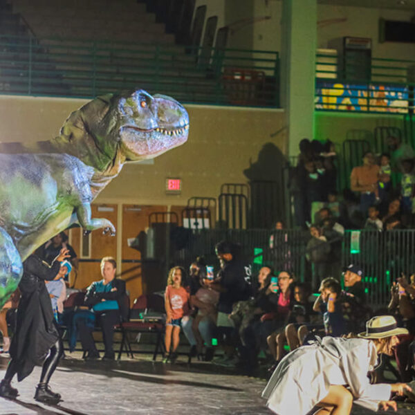 The girl in the apricot coat and the green Tyrannosaurus Rex are performing on stage