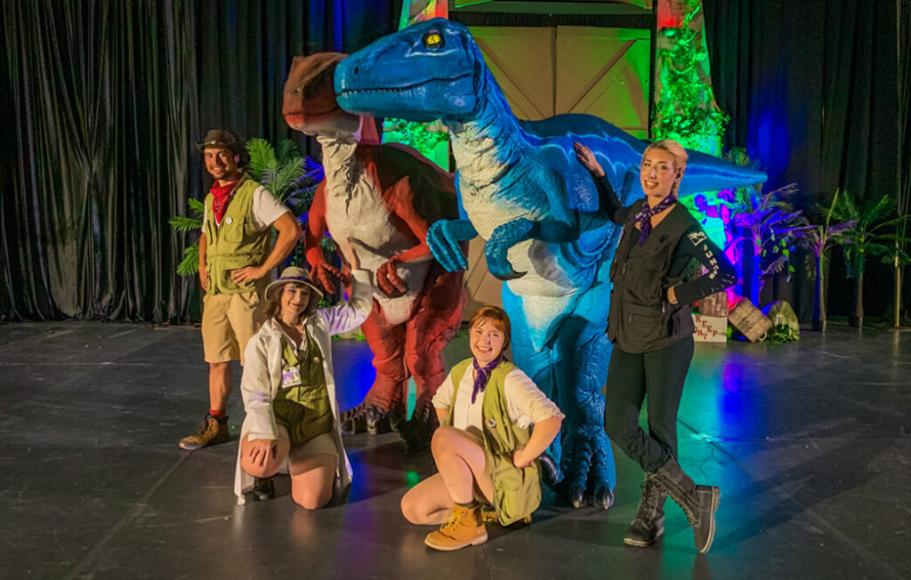 Four Worldcrafters employees pose with a blue and a red velociraptor