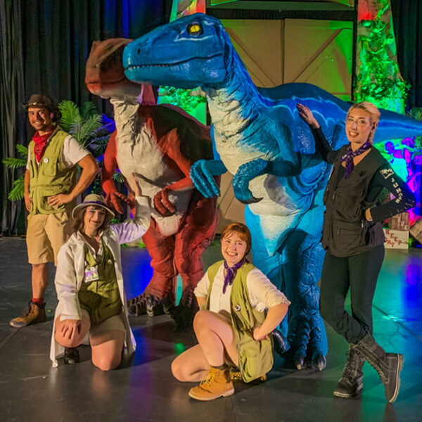 Four Worldcrafters employees pose with a blue and a red velociraptor