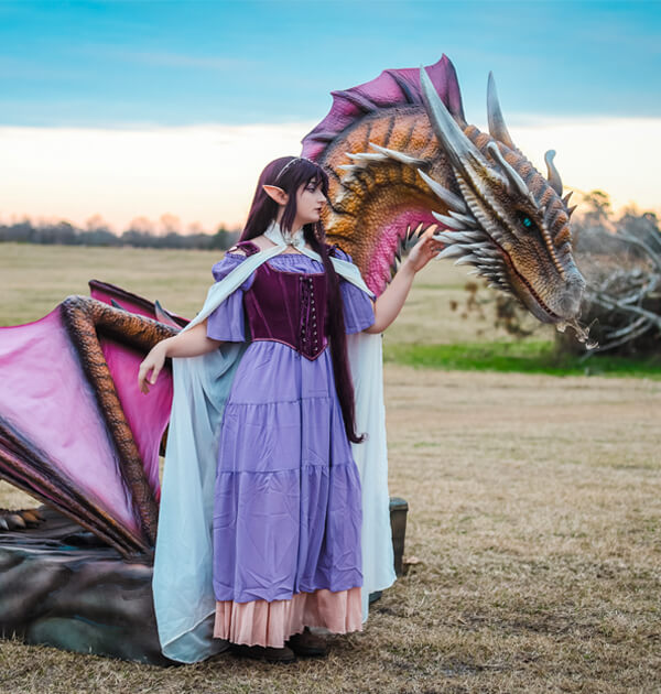 Woman in pink dress and purple robot animatronic dragon on lawn